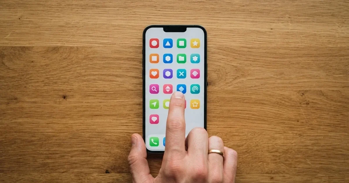 A hand tapping a smartphone screen showing generic app icons, none of them branded.